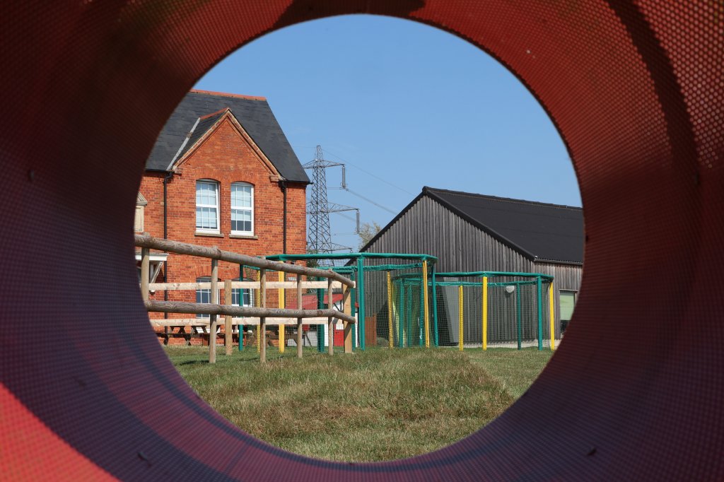 Trampolines and buildings seen through a play park tunnel.